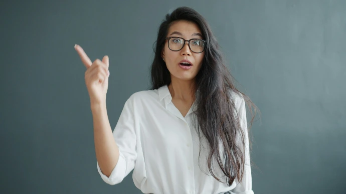Woman with glasses points her finger upwards.